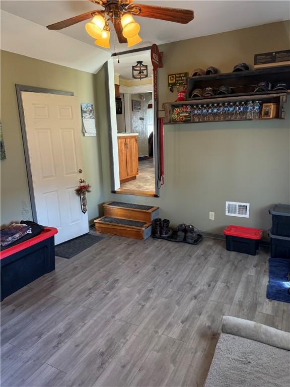 interior space featuring a wood stove, wood finished floors, visible vents, and ceiling fan