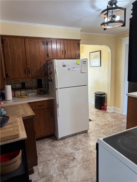 kitchen featuring ornamental molding, backsplash, white appliances, arched walkways, and light countertops