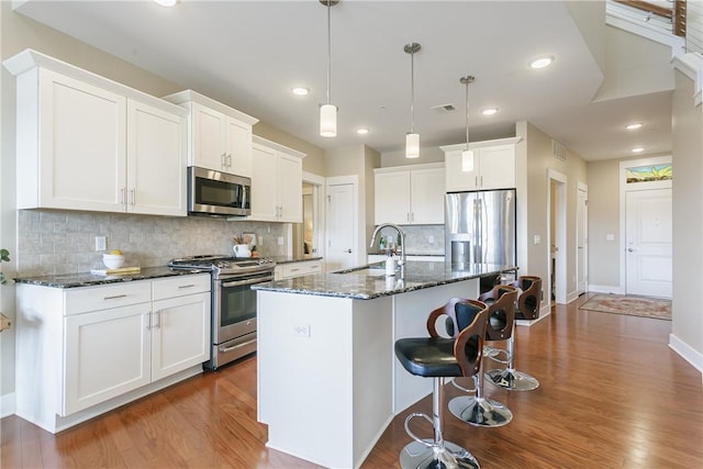 kitchen with an island with sink, appliances with stainless steel finishes, wood finished floors, white cabinets, and a sink