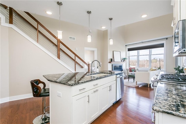 kitchen with visible vents, dark wood-type flooring, a sink, dark stone counters, and appliances with stainless steel finishes