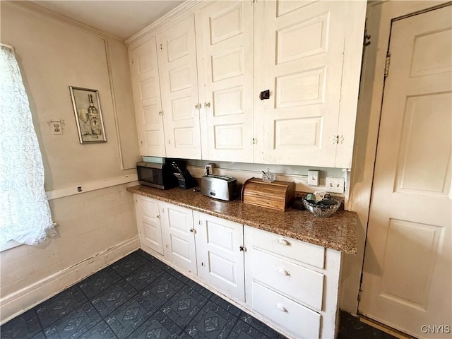 kitchen featuring stainless steel microwave, white cabinets, dark stone counters, and ornamental molding