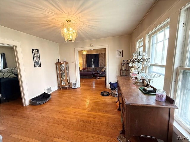 hallway with visible vents, baseboards, a chandelier, and light wood finished floors