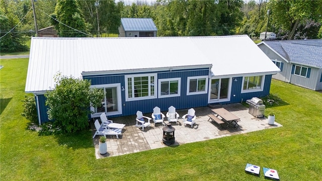 back of property with metal roof, a patio, a lawn, and a fire pit