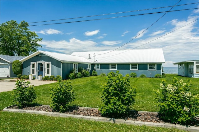 ranch-style home with a front yard, a garage, driveway, and metal roof