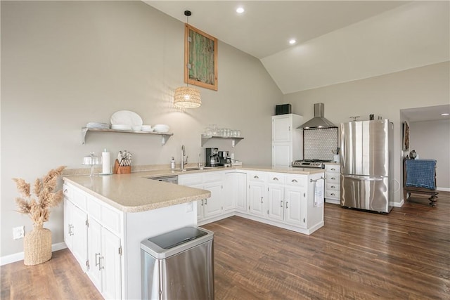 kitchen with freestanding refrigerator, a peninsula, wall chimney exhaust hood, light countertops, and lofted ceiling