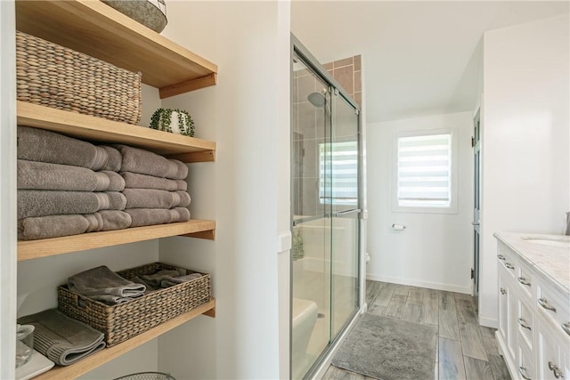 full bathroom with a shower stall, baseboards, toilet, wood finished floors, and vanity