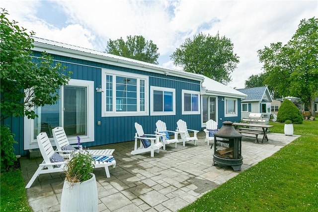 rear view of house featuring a patio, metal roof, a lawn, and an outdoor fire pit