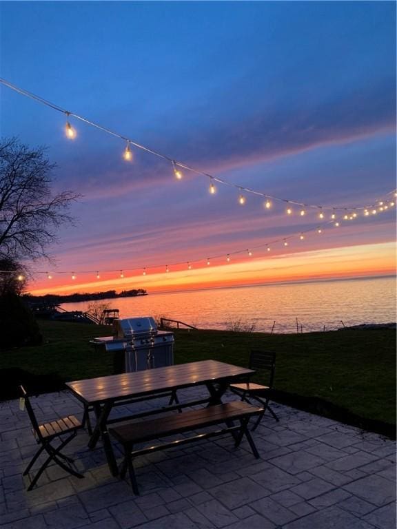 patio terrace at dusk featuring a grill, outdoor dining area, and a water view