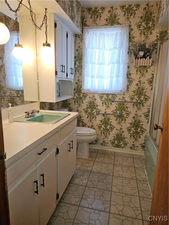 bathroom featuring toilet, vanity, and wallpapered walls