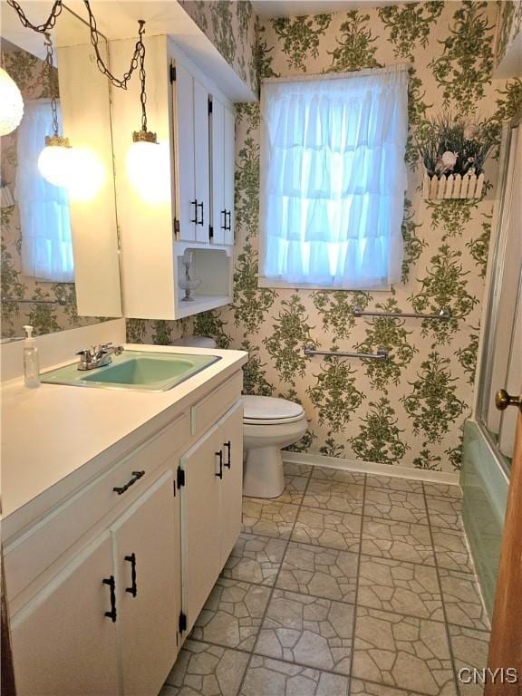 bathroom featuring vanity, a bath, baseboards, wallpapered walls, and toilet