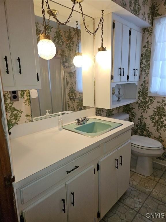 bathroom with toilet, wallpapered walls, and vanity