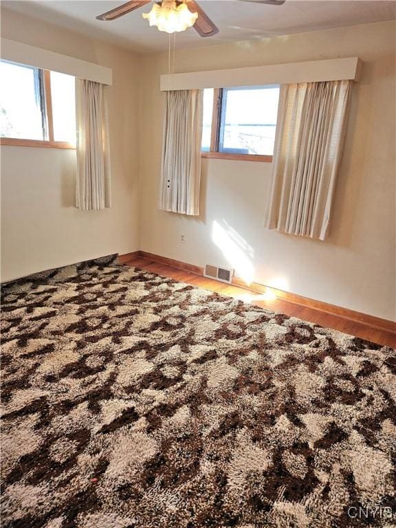 empty room with visible vents, baseboards, a ceiling fan, and wood finished floors