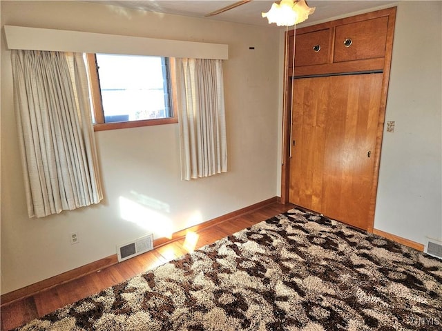 unfurnished bedroom featuring visible vents, baseboards, a closet, and wood finished floors