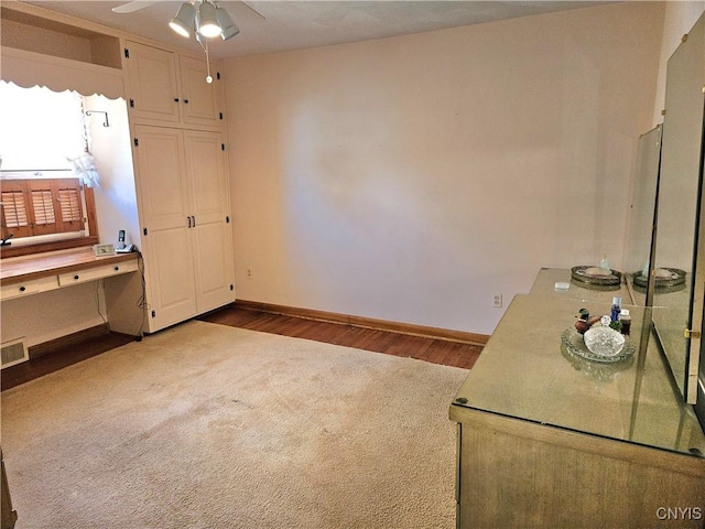 unfurnished office featuring a ceiling fan, visible vents, dark wood-style floors, baseboards, and dark colored carpet