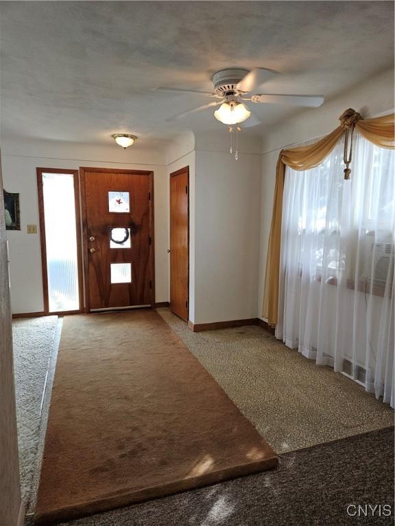 carpeted entryway with ceiling fan and baseboards