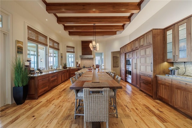 kitchen with decorative backsplash, custom exhaust hood, brown cabinetry, and light wood-style floors