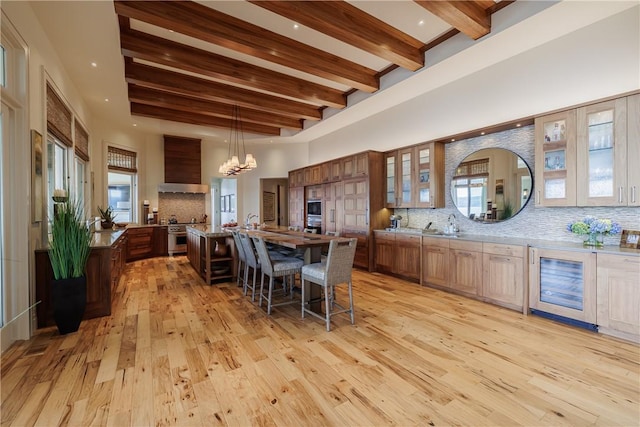 kitchen featuring premium range hood, a breakfast bar area, decorative backsplash, a towering ceiling, and light wood-style floors