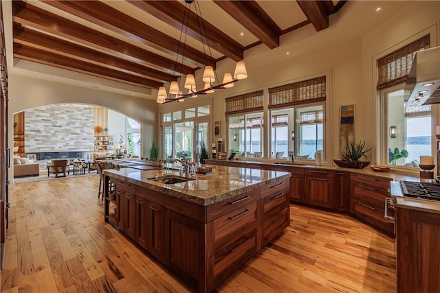 kitchen with light wood finished floors, open floor plan, beam ceiling, and a sink