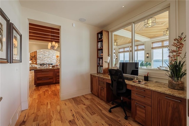 office space featuring baseboards, light wood finished floors, and built in study area