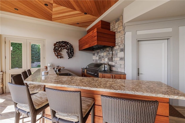 kitchen with light stone counters, a kitchen breakfast bar, wood ceiling, and a sink