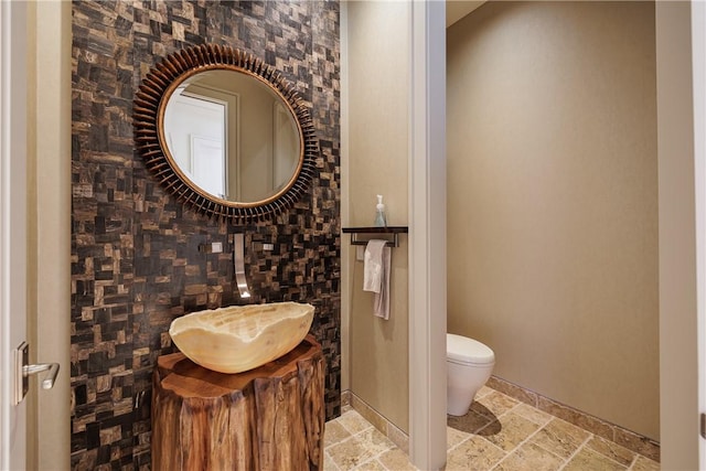 bathroom featuring a sink, toilet, and stone tile floors