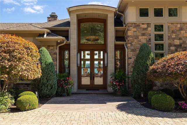 doorway to property featuring french doors, stone siding, a chimney, and stucco siding