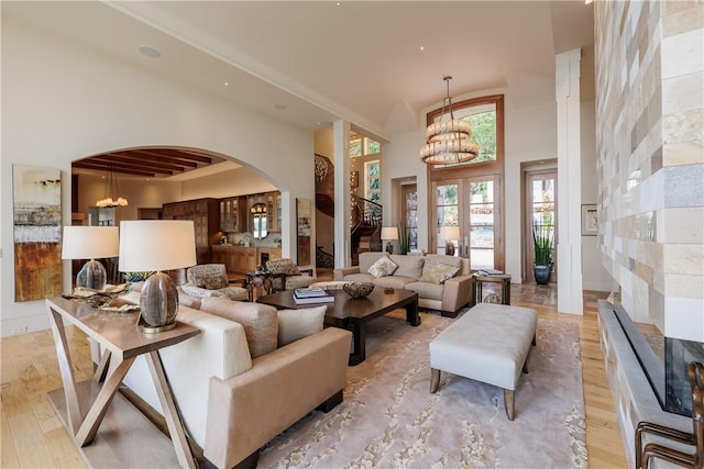 living area with an inviting chandelier, a high ceiling, light wood-style floors, and arched walkways