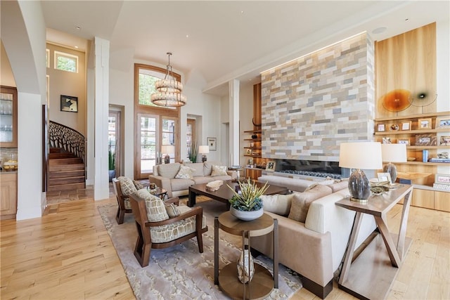 living room with stairway, light wood-type flooring, a towering ceiling, and a chandelier