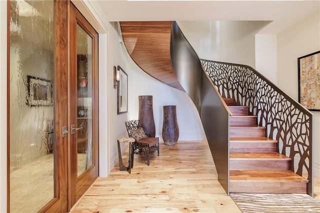 stairway featuring french doors, baseboards, and wood finished floors