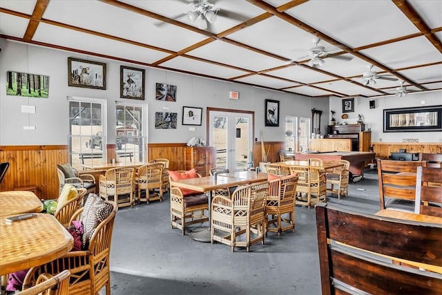 dining space with wooden walls, ceiling fan, a wainscoted wall, concrete flooring, and french doors