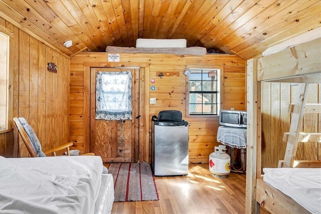 bedroom featuring fridge, wood finished floors, vaulted ceiling, wood walls, and wooden ceiling