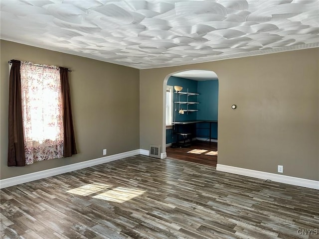 spare room with visible vents, wood finished floors, arched walkways, and baseboards