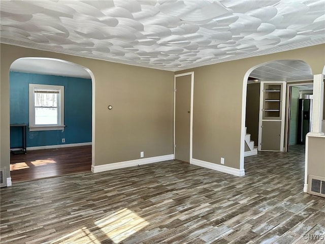 spare room with arched walkways, baseboards, and wood finished floors