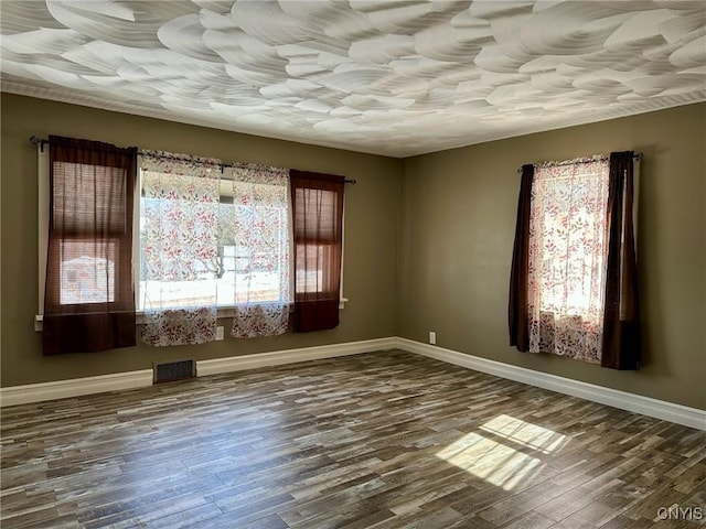 unfurnished room with wood finished floors, visible vents, and baseboards