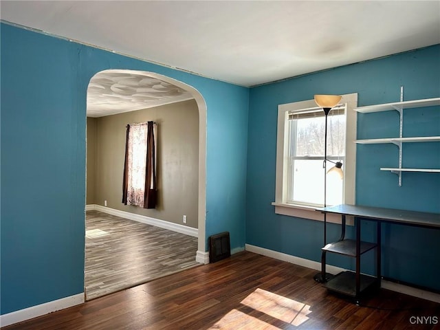 interior space with baseboards, arched walkways, and wood finished floors