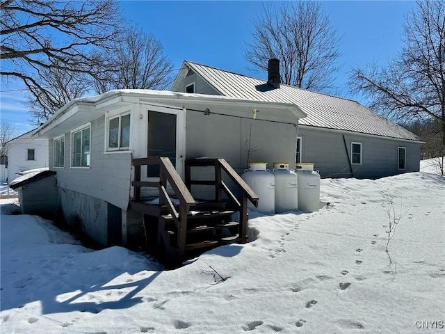 snow covered property with a standing seam roof, a chimney, and metal roof