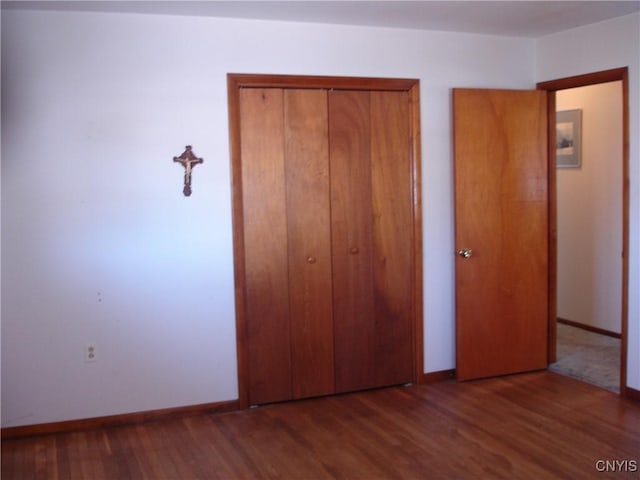 unfurnished bedroom featuring wood finished floors, a closet, and baseboards