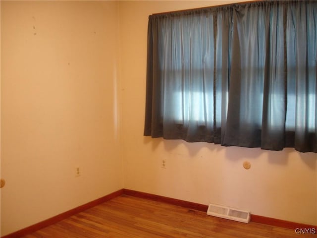 unfurnished room with wood finished floors, baseboards, and visible vents