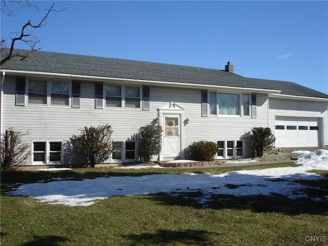 split foyer home featuring an attached garage, a chimney, and a front lawn