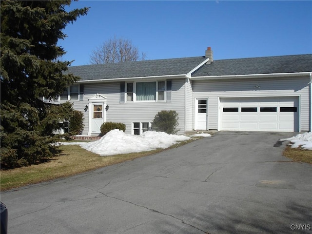 raised ranch featuring an attached garage, a chimney, driveway, and a shingled roof