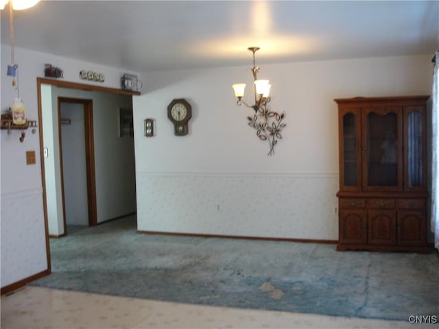 unfurnished dining area featuring wallpapered walls, a notable chandelier, carpet, and a wainscoted wall