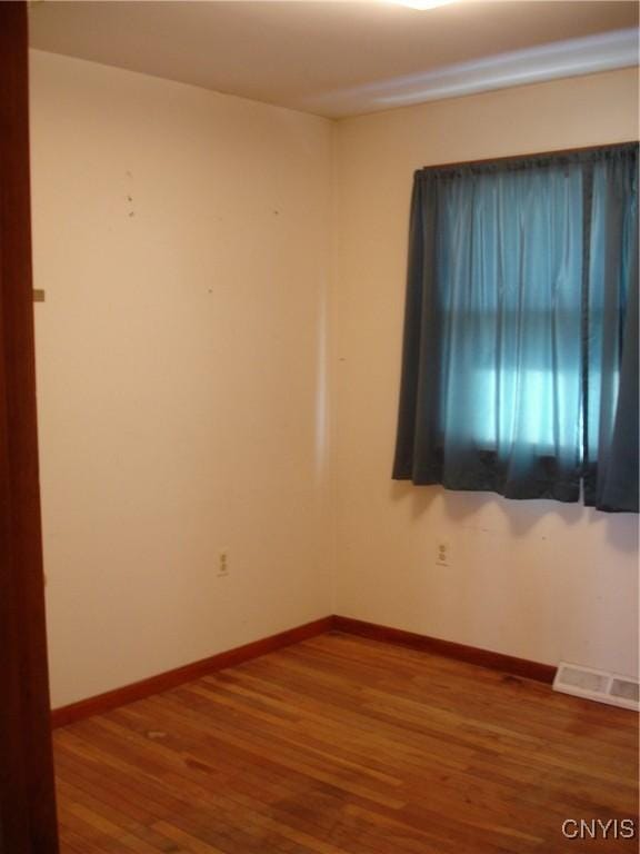 empty room with wood finished floors, visible vents, and baseboards