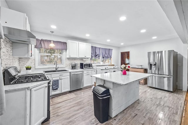 kitchen featuring light wood finished floors, tasteful backsplash, a center island, stainless steel appliances, and a sink