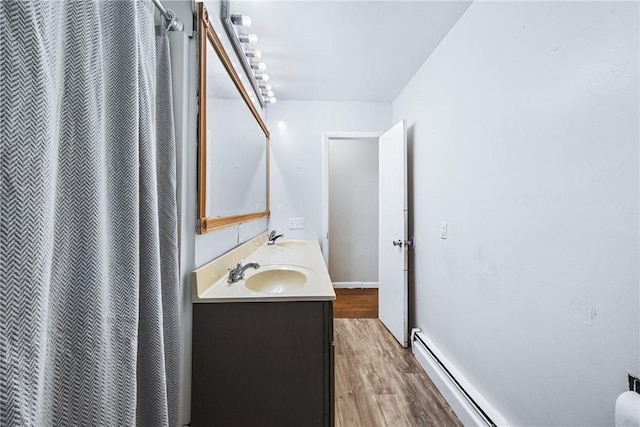 full bath with double vanity, wood finished floors, a baseboard heating unit, and a sink