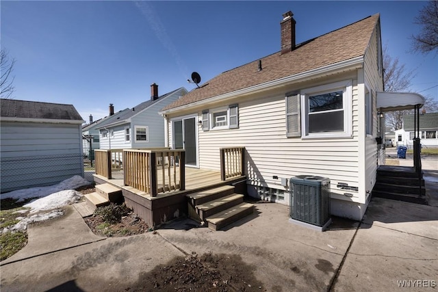 back of property with central air condition unit, roof with shingles, a wooden deck, and a chimney