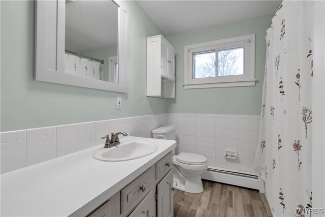 bathroom with tile walls, toilet, wood finished floors, vanity, and a baseboard radiator