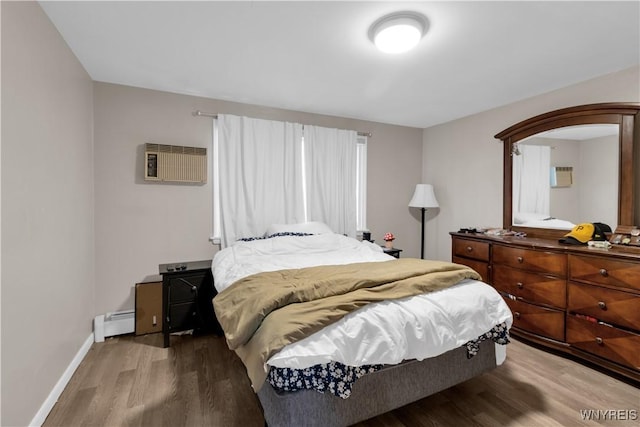 bedroom featuring a baseboard heating unit, wood finished floors, baseboards, and a wall mounted air conditioner