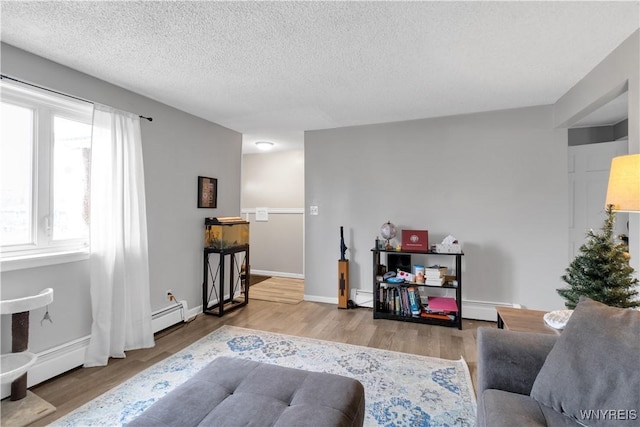 living room with a textured ceiling, a baseboard heating unit, baseboards, and wood finished floors