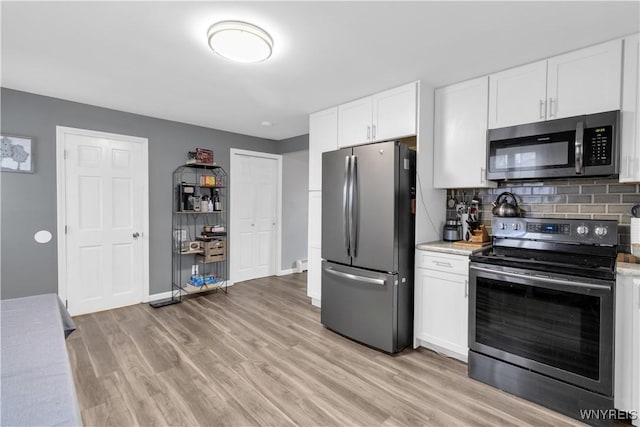 kitchen with light wood-type flooring, tasteful backsplash, white cabinetry, appliances with stainless steel finishes, and light countertops