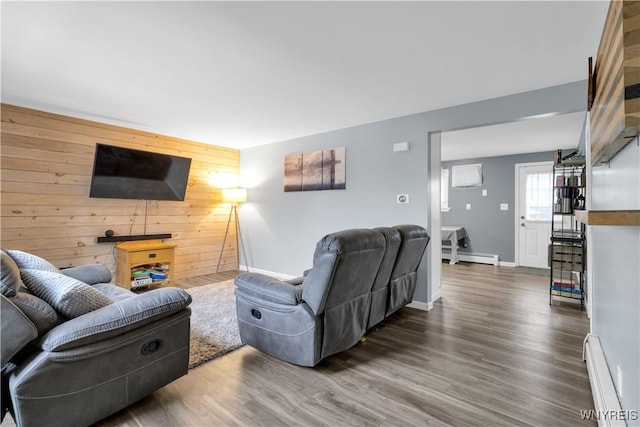 living area with an accent wall, wooden walls, wood finished floors, and a baseboard radiator